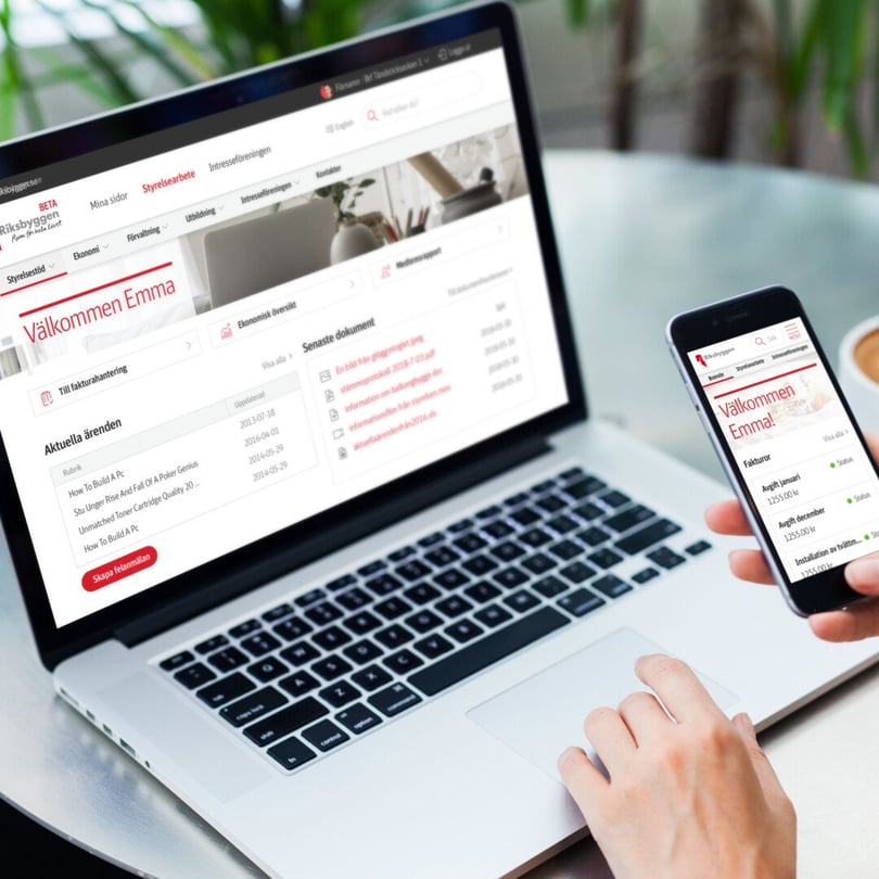 Händer som använder en bärbar dator och smartphone med en bankwebbplats eller app öppen, mot en bakgrund av en bordsyta och gröna växter