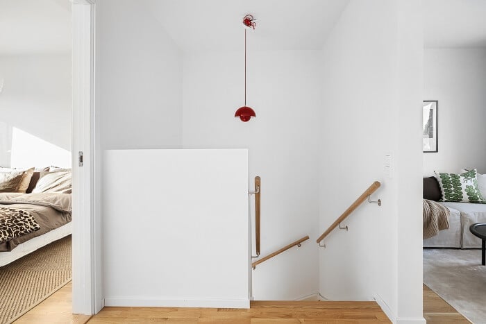 Trappa med vita väggar, träräcken och en röd taklampa, med en säng och en soffa synliga i bakgrunden