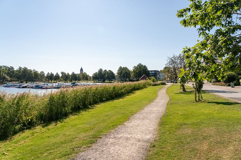 Promenadväg i Strängnäs längs vattnet med grön park, båtar och träd under klar himmel