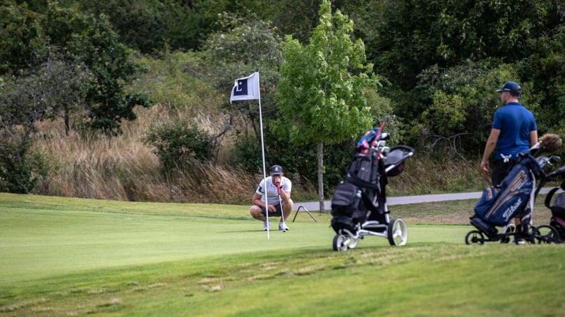 Golfspelare i vitt som puttar vid flaggan på en golfbana, med två golfvagnar i förgrunden