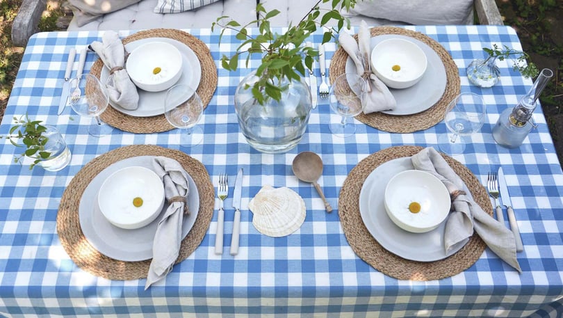 Uppdukat bord med blåvitrutig duk, tallrikar, glas, bestick och blomvaser utomhus