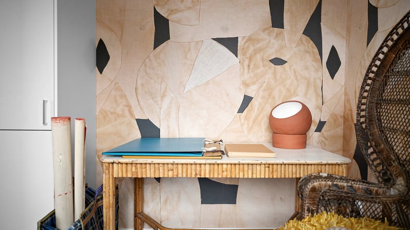 Interiör med skrivbord, lampor och flätad stol i ett rum med mönstrad tapet