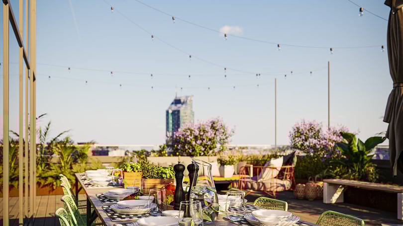 Uteservering med dukat bord, växter och utsikt mot stadens skyline under klar himmel