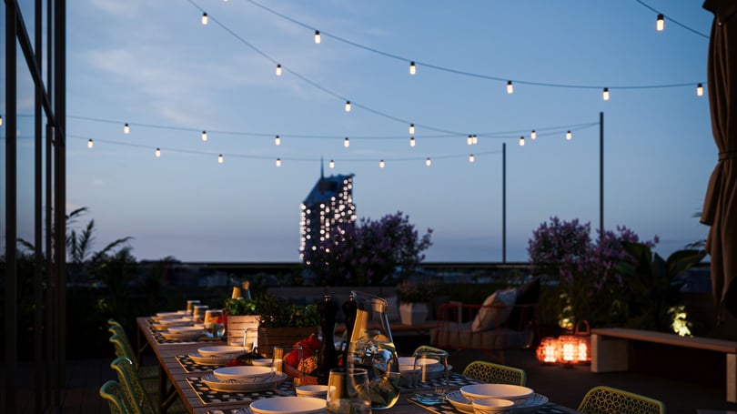 Uppdukad utomhusmiddag på en terrass i skymningen med ljusslingor och dukat långbord