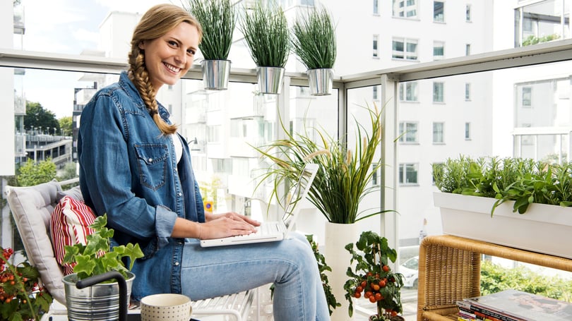 Kvinna som sitter på en inglasad balkong med laptop, omgiven av gröna växter