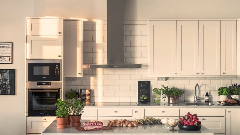 Lägenhet med modernt kök, vita skåpluckor, inbyggd ugn och mikro samt köksö med grönsaker och växter