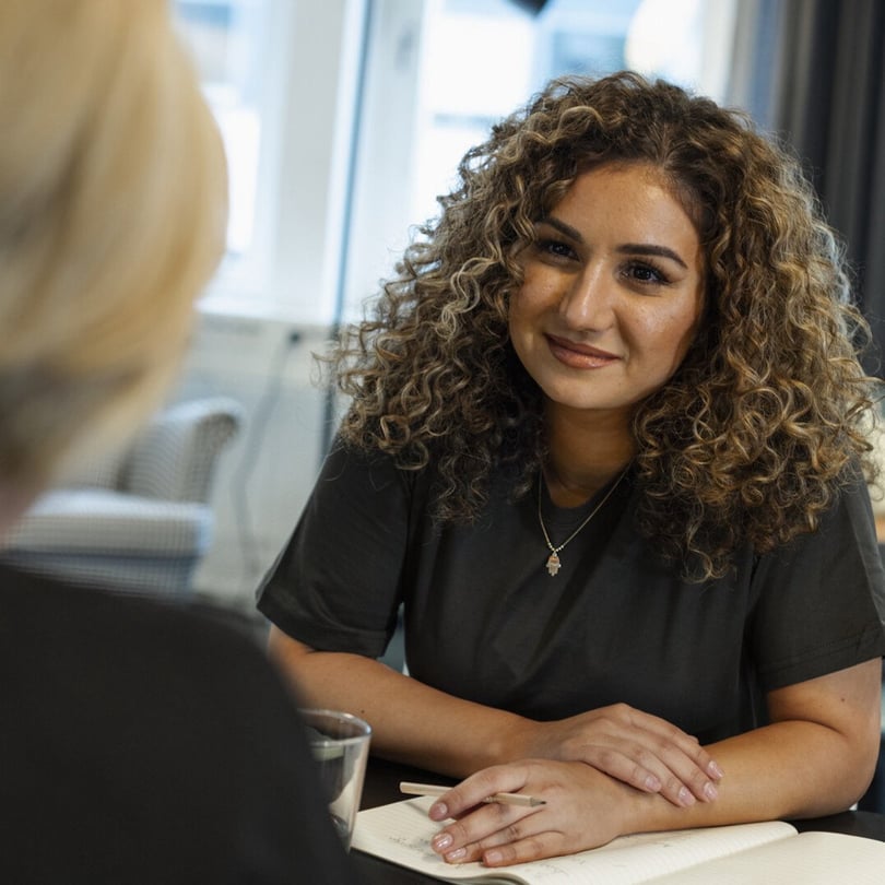 Porträtt av en kvinna med lockigt hår i svart tröja vid ett bord