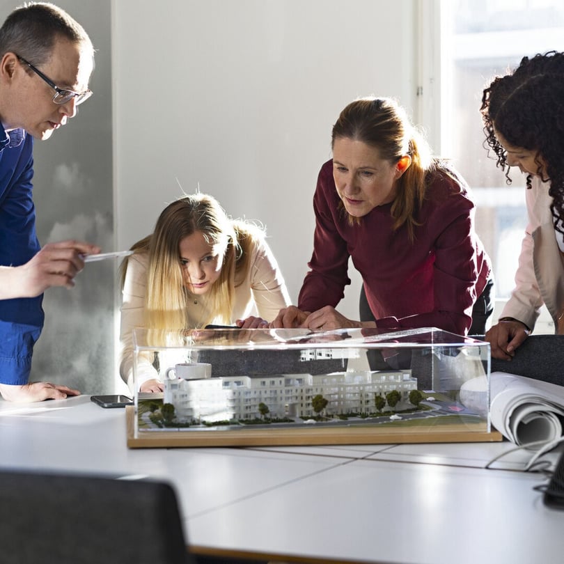 Fyra personer lutar sig över en modell av ett bostadshus under ett möte