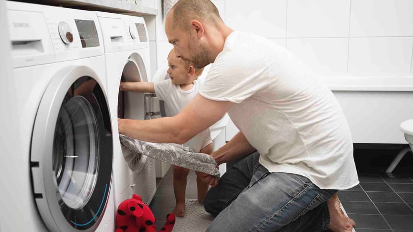En man och ett barn laddar en tvättmaskin i ett tvättrum