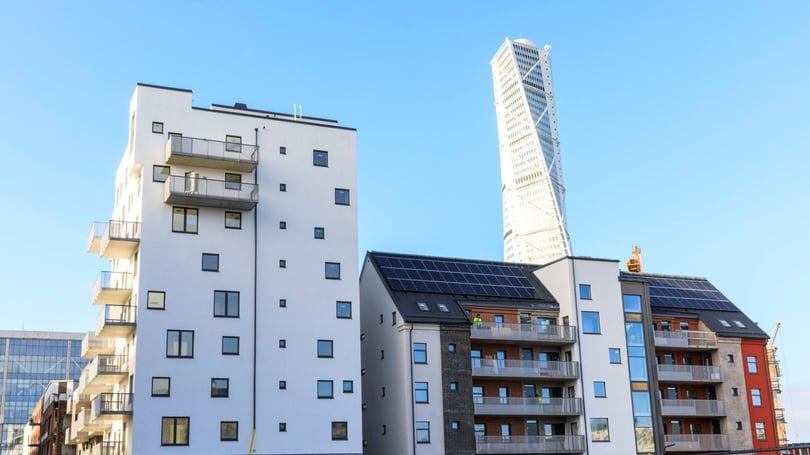 Flerbostadshus med balkonger och solpaneler mot blå himmel