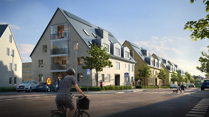 Modernt bostadsområde med radhus och lägenheter, cyklist på en gata i förgrunden och människor som promenerar