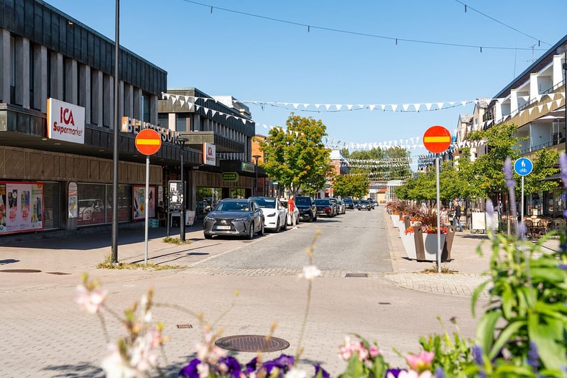 Gata i Strängnäs med butiker, parkerade bilar och blomsterlådor under klarblå himmel