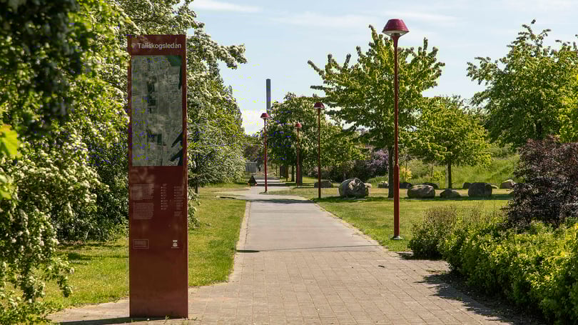 Promenadstig i grön parkmiljö i Helsingborg med skylt och röda gatlyktor längs gångvägen