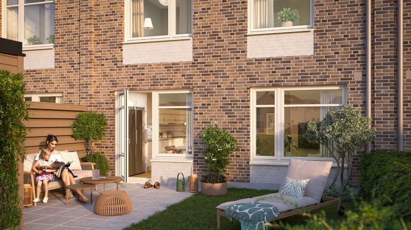 En kvinna och ett barn sitter på en soffa på en uteplats framför ett tegelhus