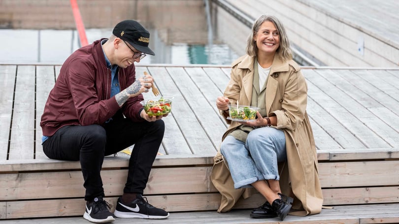 Två personer sitter utomhus och äter sallad