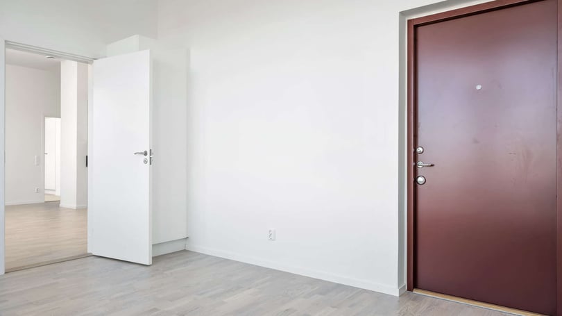 Inflyttningsklar lägenhet med ljusa väggar, grått golv och brun ytterdörr