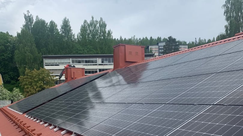 Solceller på ett lutande tak med röda takkupor och träd i bakgrunden