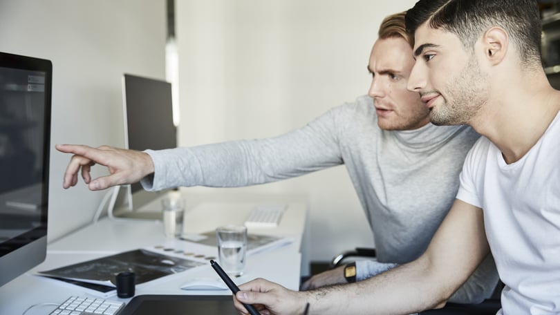 Två personer vid en dator i ett kontorsliknande rum, varav den ena pekar mot skärmen