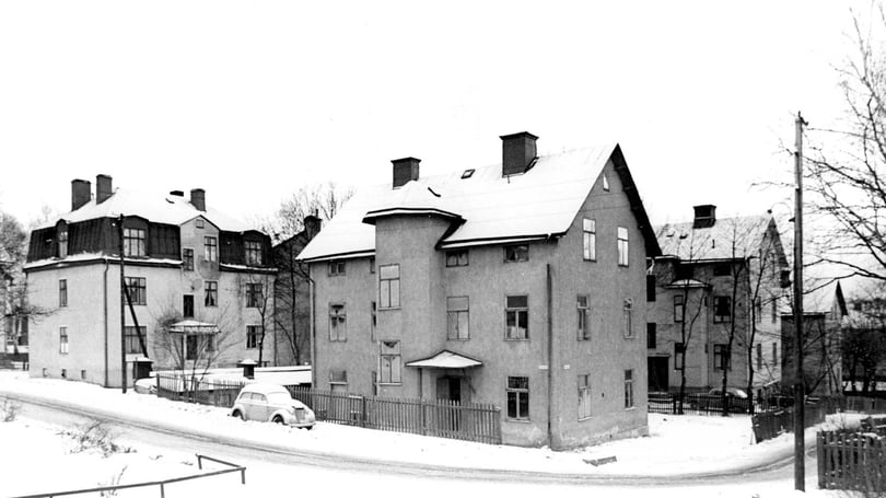 Snötäckt bostadshus i ett bostadsområde med flera flerfamiljshus och en parkerad bil