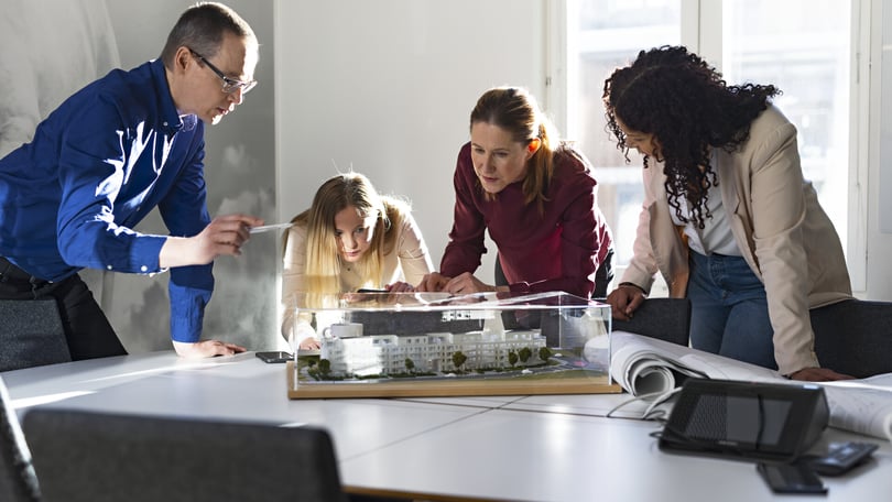 Fyra personer samlade runt en byggmodell på ett bord