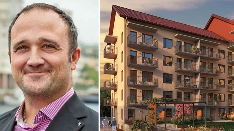 Porträtt av en man i kostym och rosa skjorta. Gårdsmiljö med flerbostadshus och balkonger i kvällsljus