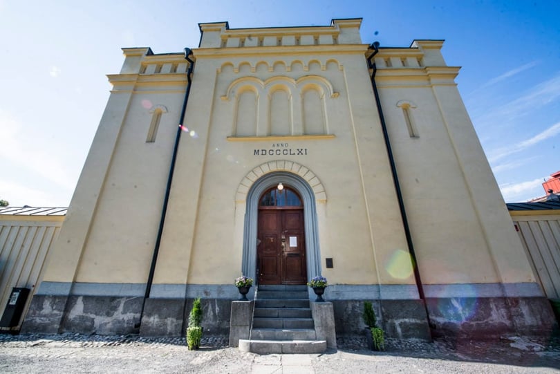 Fasad på historisk byggnad med välvd entré och trappa, sedd framifrån i dagsljus