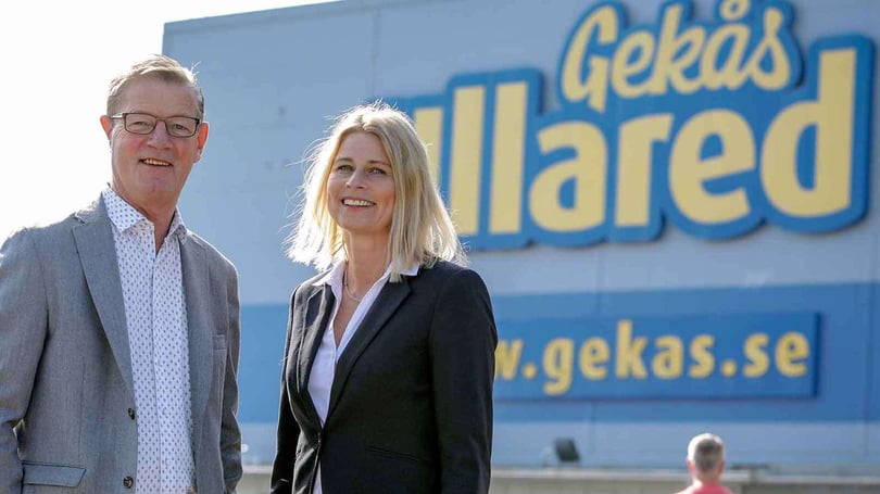 Två personer står framför en blå Gekås Ullared-skylt