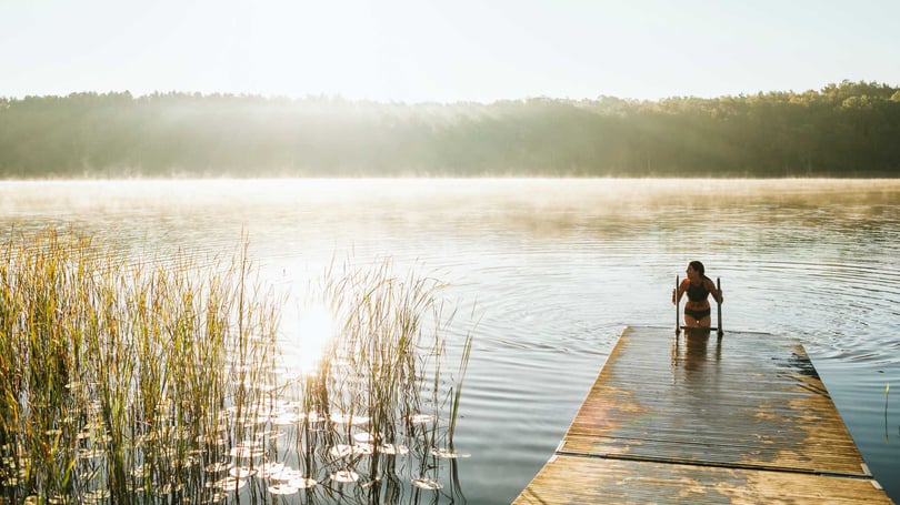 Kvinna badar från en brygga i en stilla sjö i morgondimma