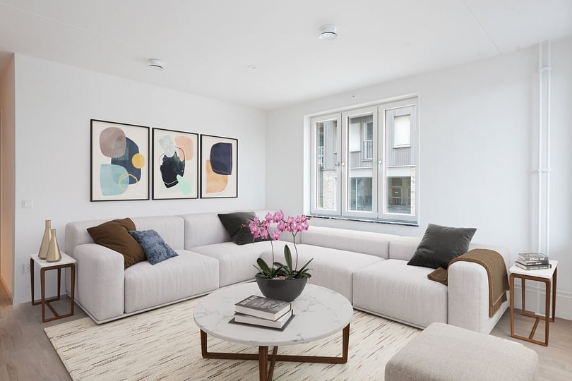 Ljust och stilrent vardagsrum med ljus L-formad soffa, abstrakt väggkonst, marmorbord och stora fönster