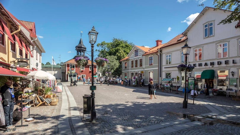 Stadsgata med butiker, historiska hus och människor på ett torg i solsken