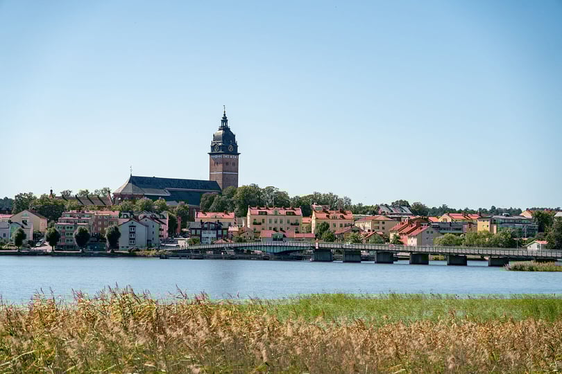 Utsikt över Strängnäs vid vatten med kyrktorn, bro och färgglada hus i solsken