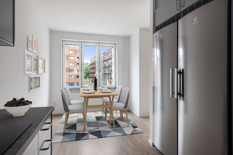 Kök med matplats, ljus inredning, kylskåp i rostfritt stål och utsikt mot bostadshus genom stort fönster