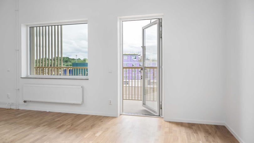 Inflyttningsklart rum med ljusa väggar, trägolv och stora fönster samt balkongdörr