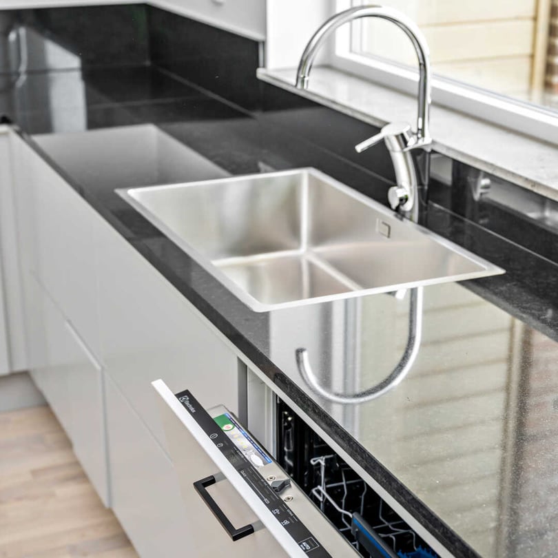 Inflyttningsklar lägenhet med kök, svart bänkskiva, diskho och diskmaskin