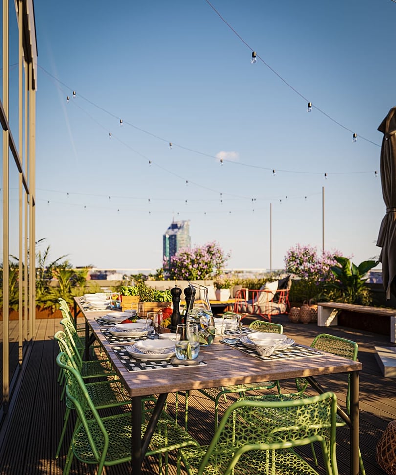 Uppdukat matbord på en takterrass med gröna stolar, växter och utsikt över stadssilhuetten