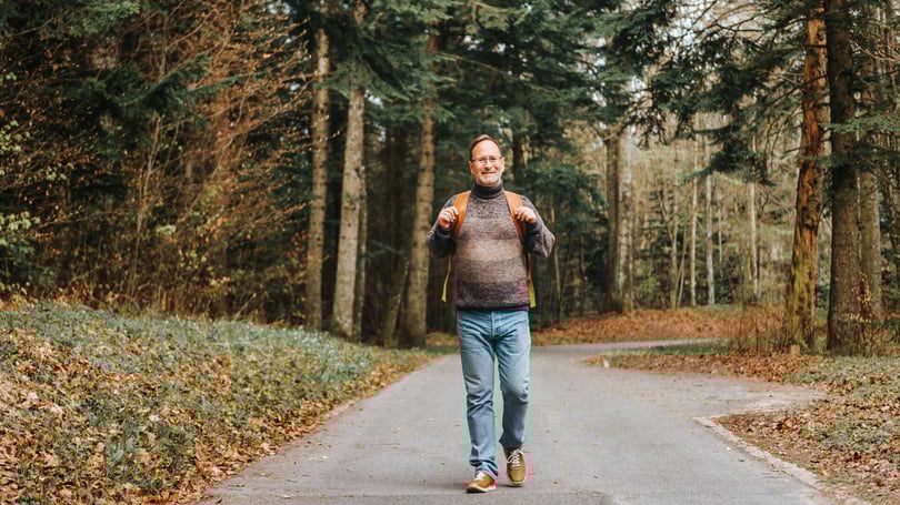 En man med ryggsäck promenerar på en skogsväg