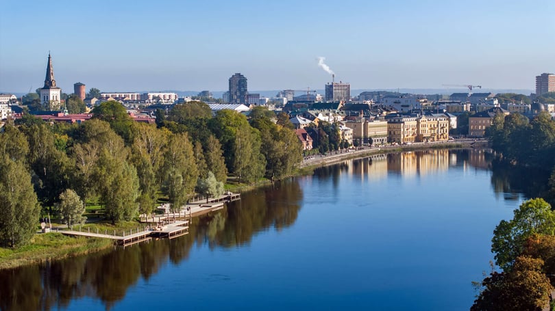 Utsikt över Karlstad med en bred älv, trädkantad strandpromenad och byggnader längs vattnet