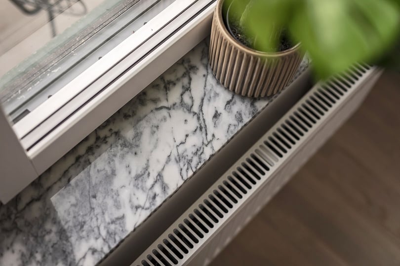 Fönsterbänk i marmor med växtkruka och element under fönstret