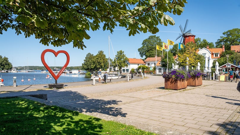 Hamnpromenad  i Strängnäs med hjärtformad skulptur, båtar, flaggor och en väderkvarn i solsken