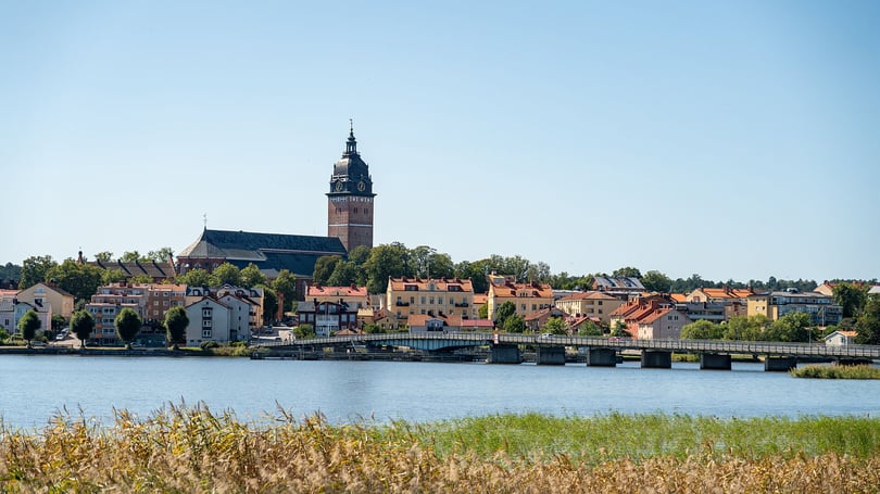 Vy över Strängnäs  med kyrktorn, bro över vatten och färgglada hus längs strandkanten