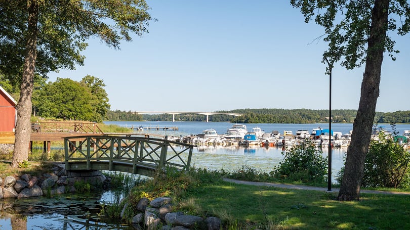 Brygga vid en småbåtshamn i Strängnäs  med båtar, grönska och en bro i bakgrunden