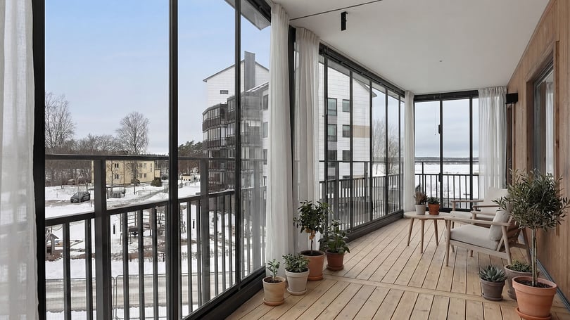 Inglasad balkong med ljusa sittmöbler, växter och utsikt över snötäckt område