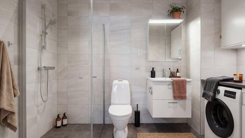 Badrum med dusch, toalett, handfat och tvättmaskin i ljusa kaklade ytor