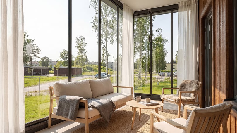 Inflyttningsklar lägenhet med ljus vardagsrumsdel, stora fönster och utsikt mot grönområde