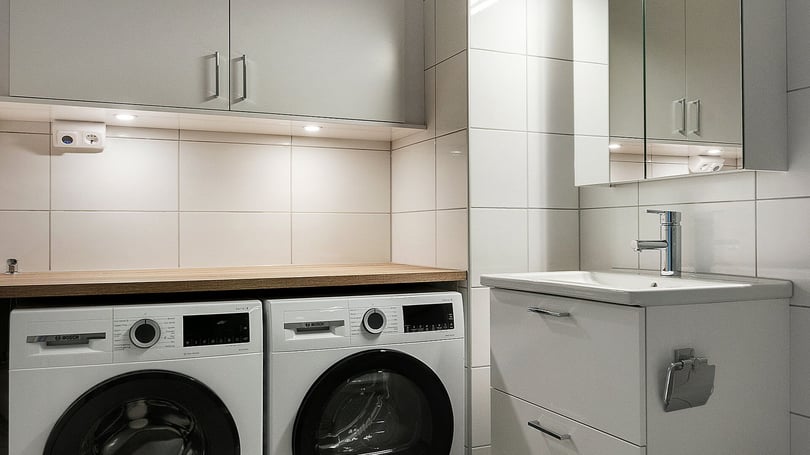 Badrum med två frontmatade tvättmaskiner, arbetsbänk och handfat med spegelskåp