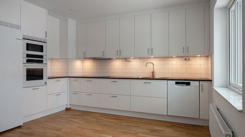 Inflyttningsklar lägenhet med modernt vitt kök, integrerade vitvaror och trägolv