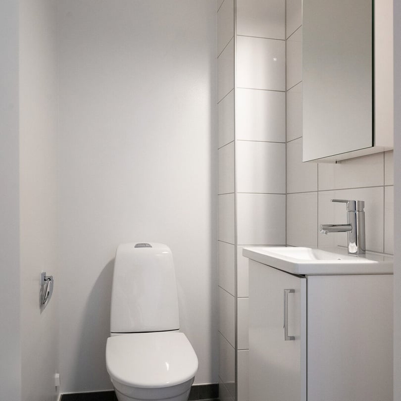 Litet, helkaklat badrum med toalett, handfat och spegelskåp i vitt