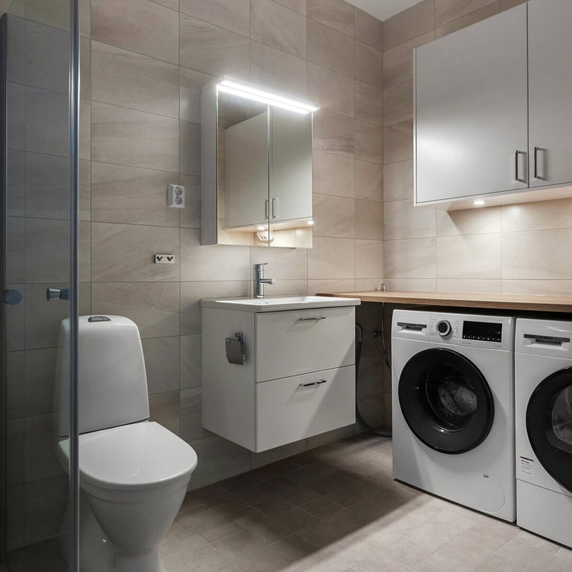Modernt badrum med toalett, tvättställ med spegelskåp och tvättmaskiner under bänkskiva