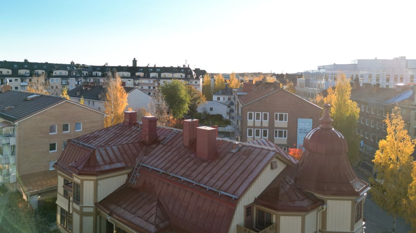 Utsikt över bostadskvarter med flerbostadshus, höstfärgade träd och en äldre byggnad med rött plåttak