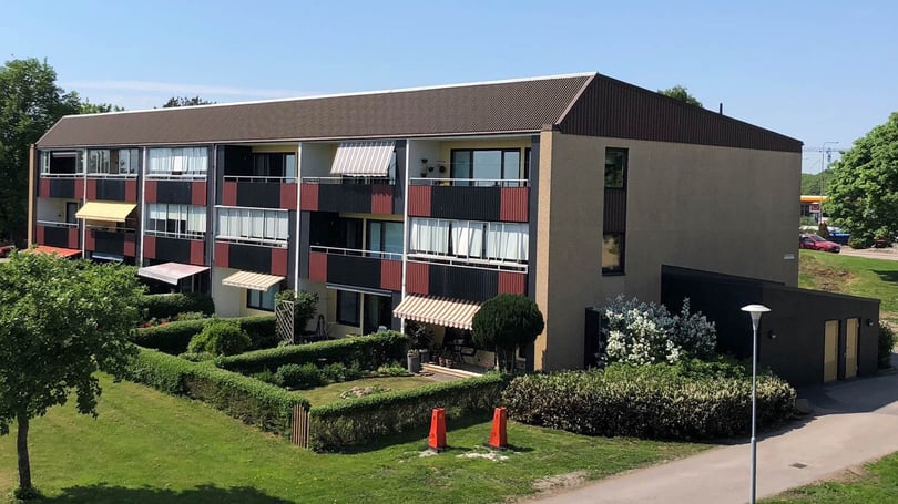 Flerbostadshus med balkonger och välskötta häckar i en grön utemiljö